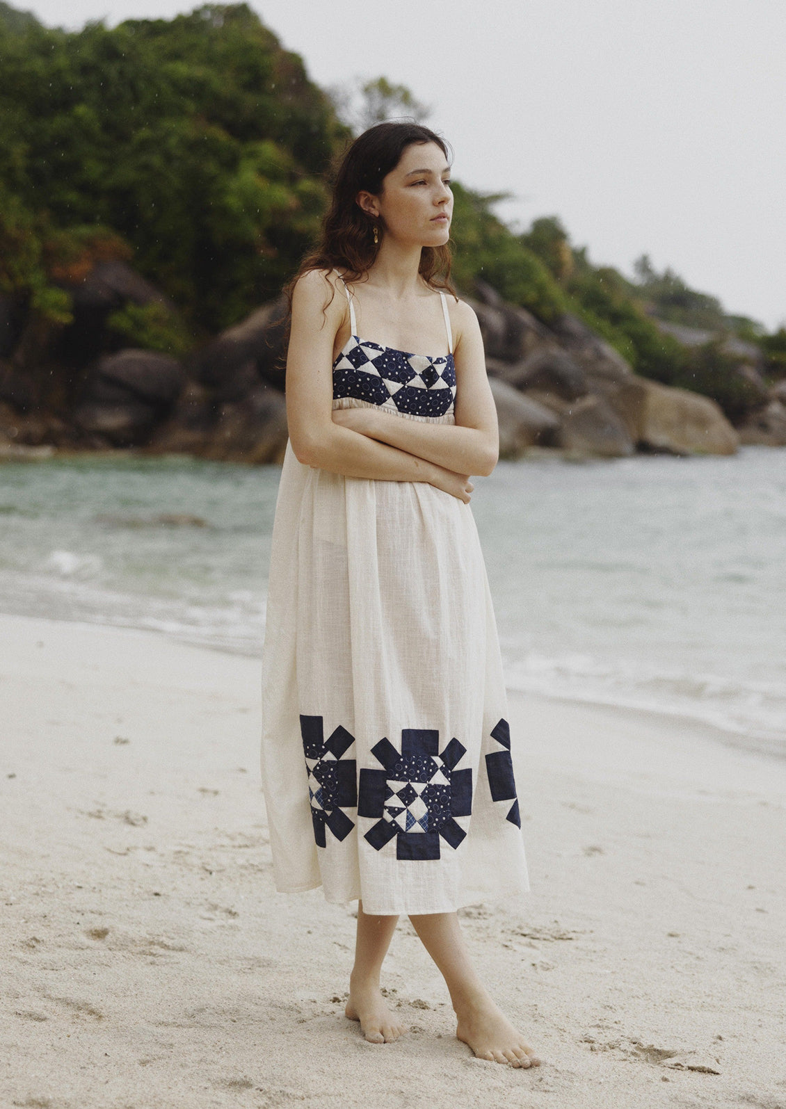 A woman wearing a long white sundress with indigo patchwork quilting details.