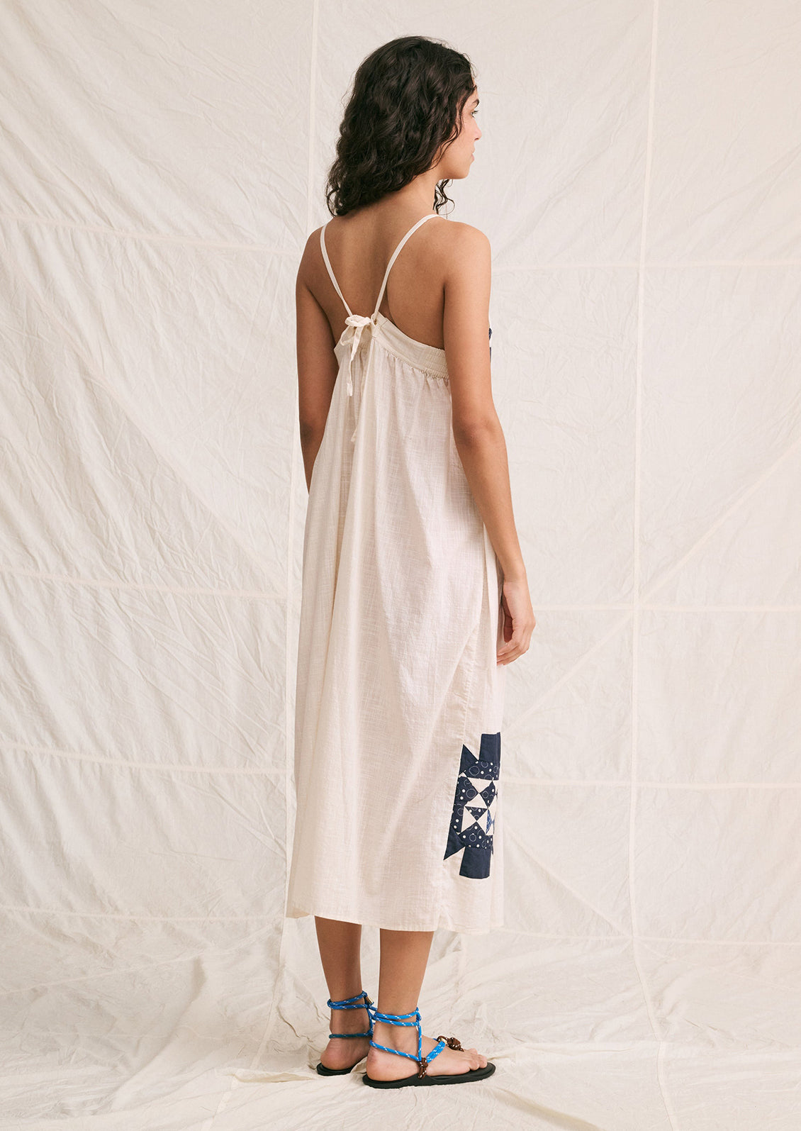 A woman wearing a long white sundress with indigo patchwork quilting details.