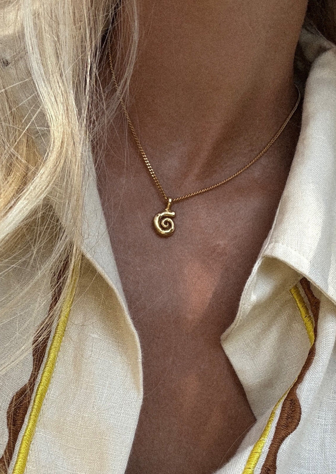 Gold spiral necklace worn by a person with a neutral background