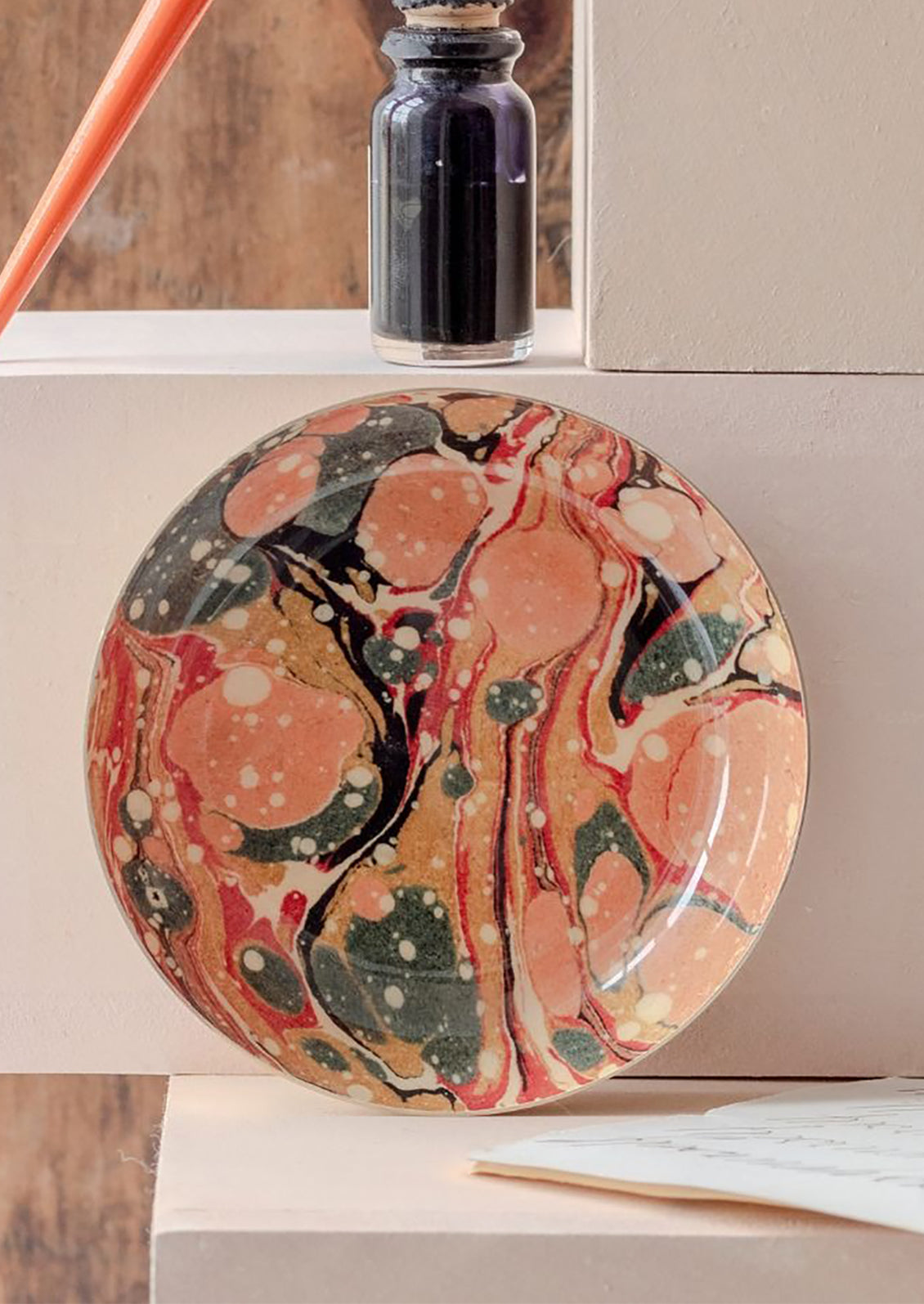 Round marbled patterned tray on a wooden surface with a bottle of ink in the background.