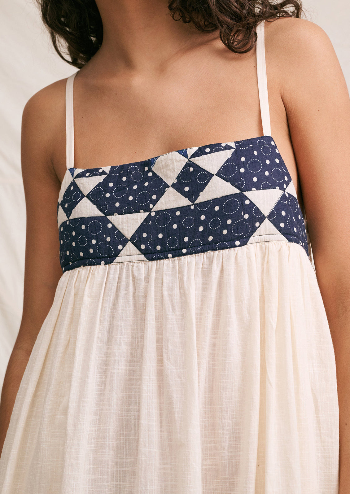 A woman wearing a long white sundress with indigo patchwork quilting details.