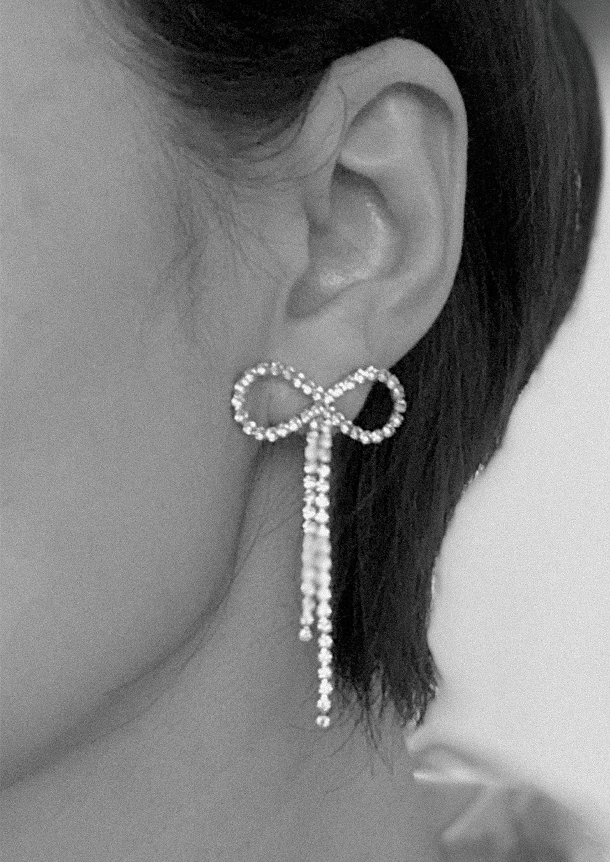 Close-up of an ear wearing a decorative bow-shaped earring with dangling elements.