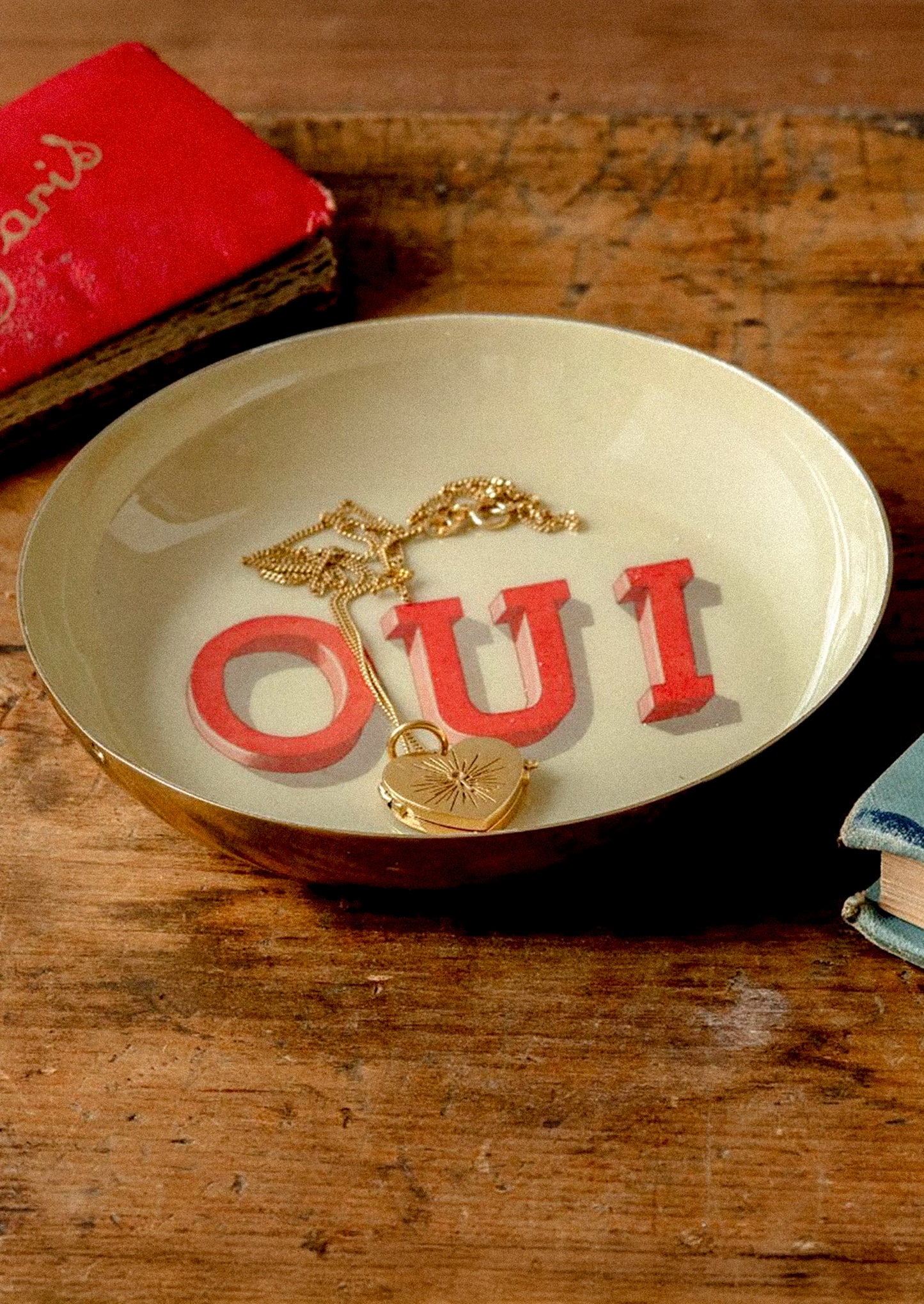Tray with 'OUI' letters and a gold necklace on a wooden surface