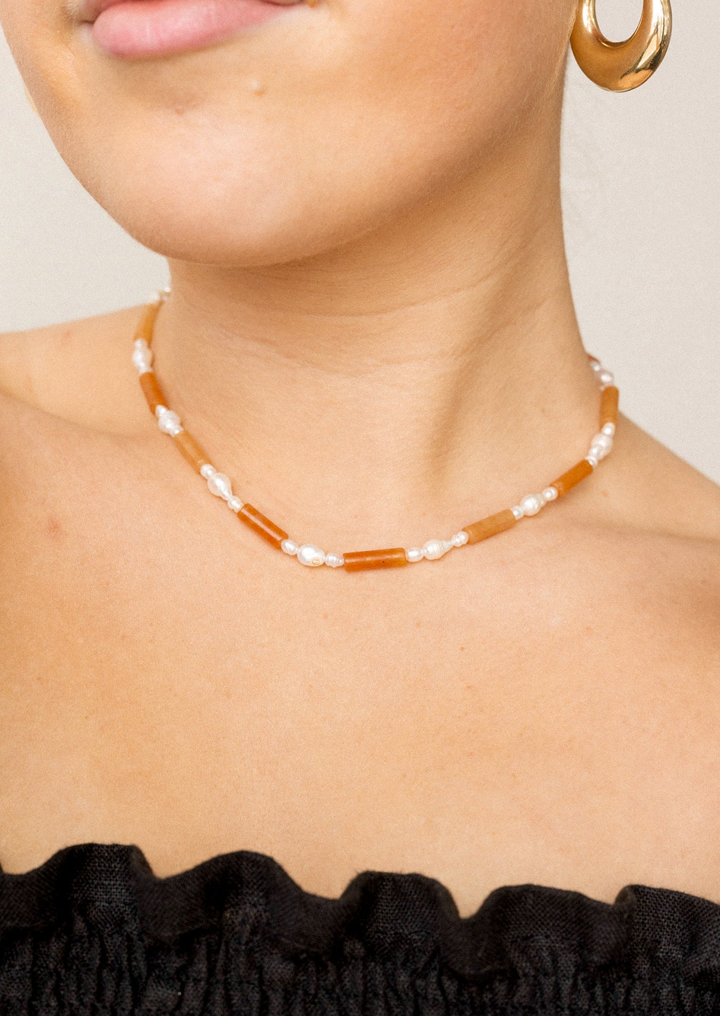 Necklace with orange beads and pearls worn by a person against a neutral background