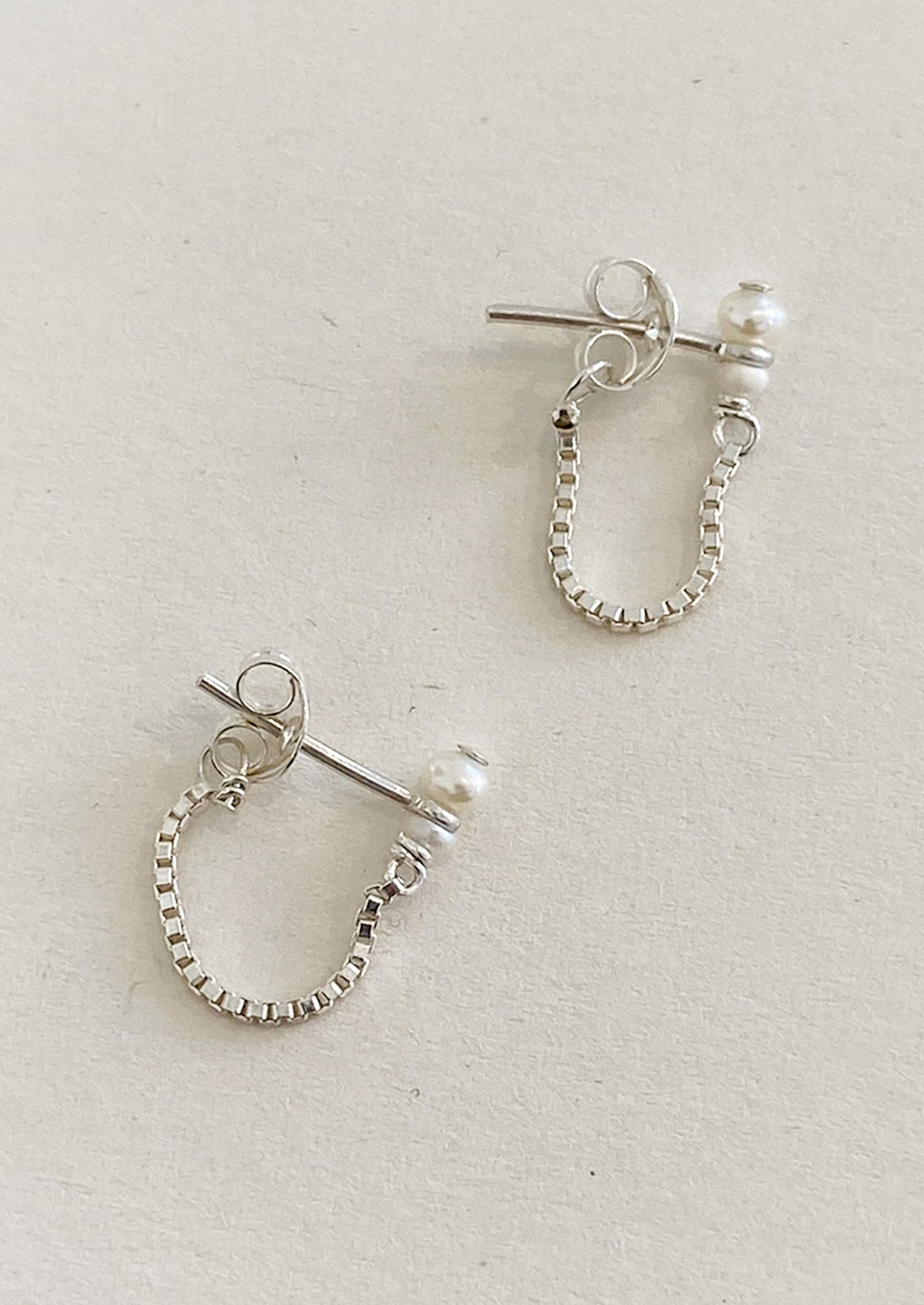 Silver hoop earrings with pearl accents on a light gray background