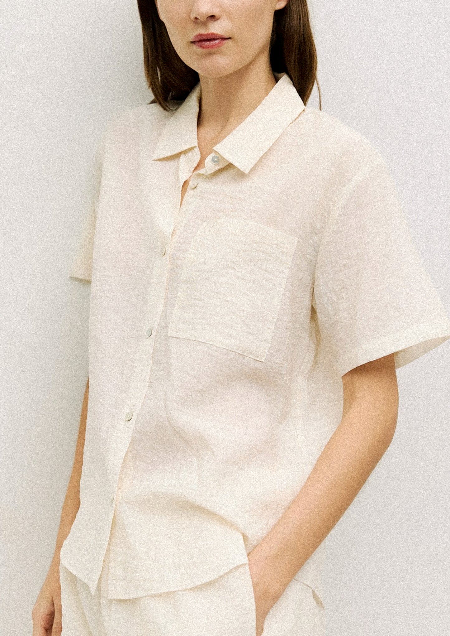 A woman wearing a short sleeve collared button front shirt in cream with soft wrinkled texture.