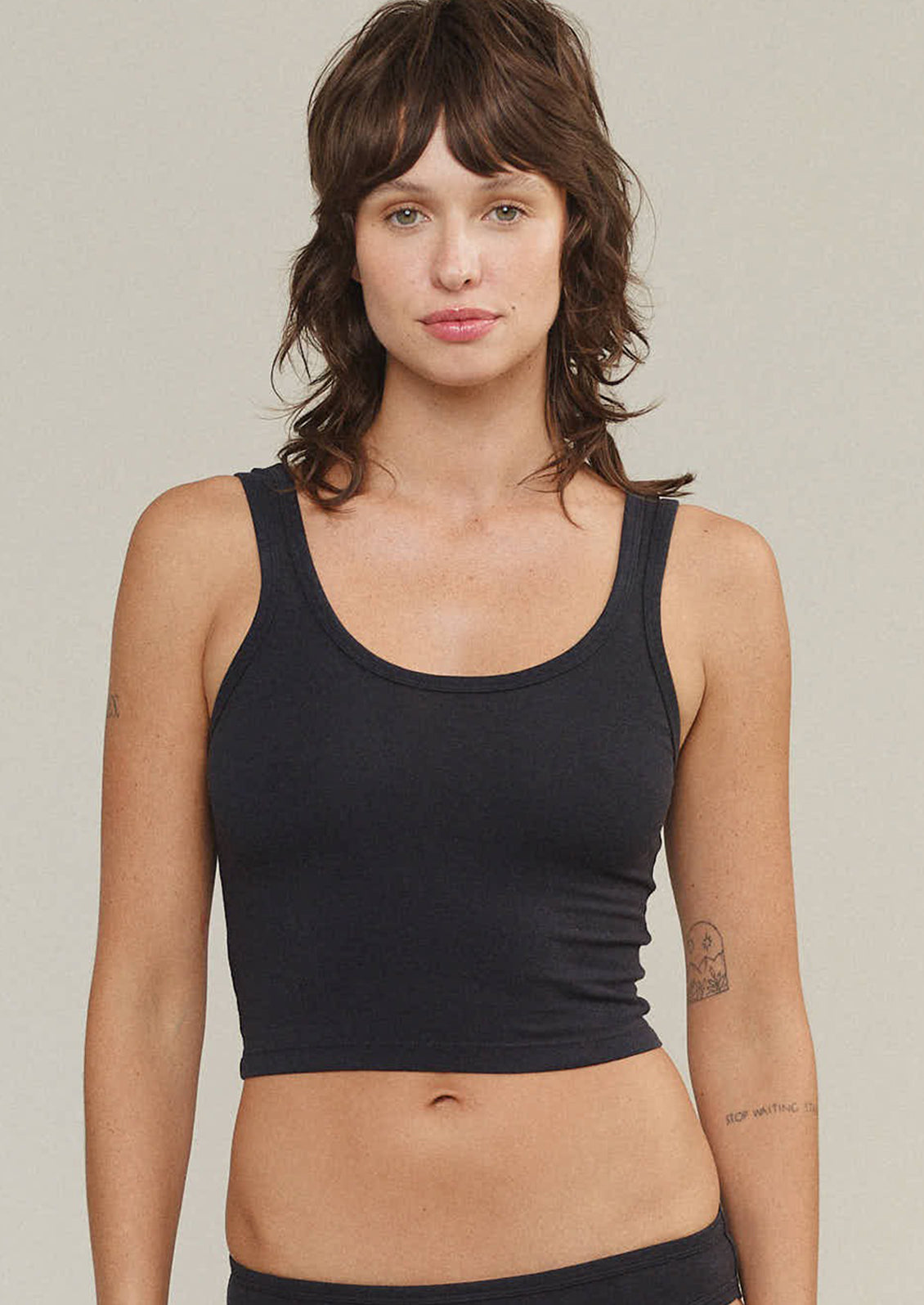 A woman wearing a cropped, fitted scoop neck tank top in black.