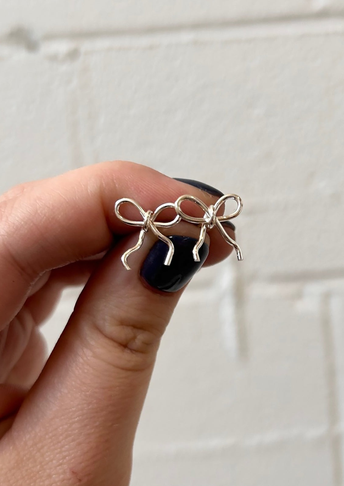 A pair of small handmade earrings in bow shape made from sterling silver wire.