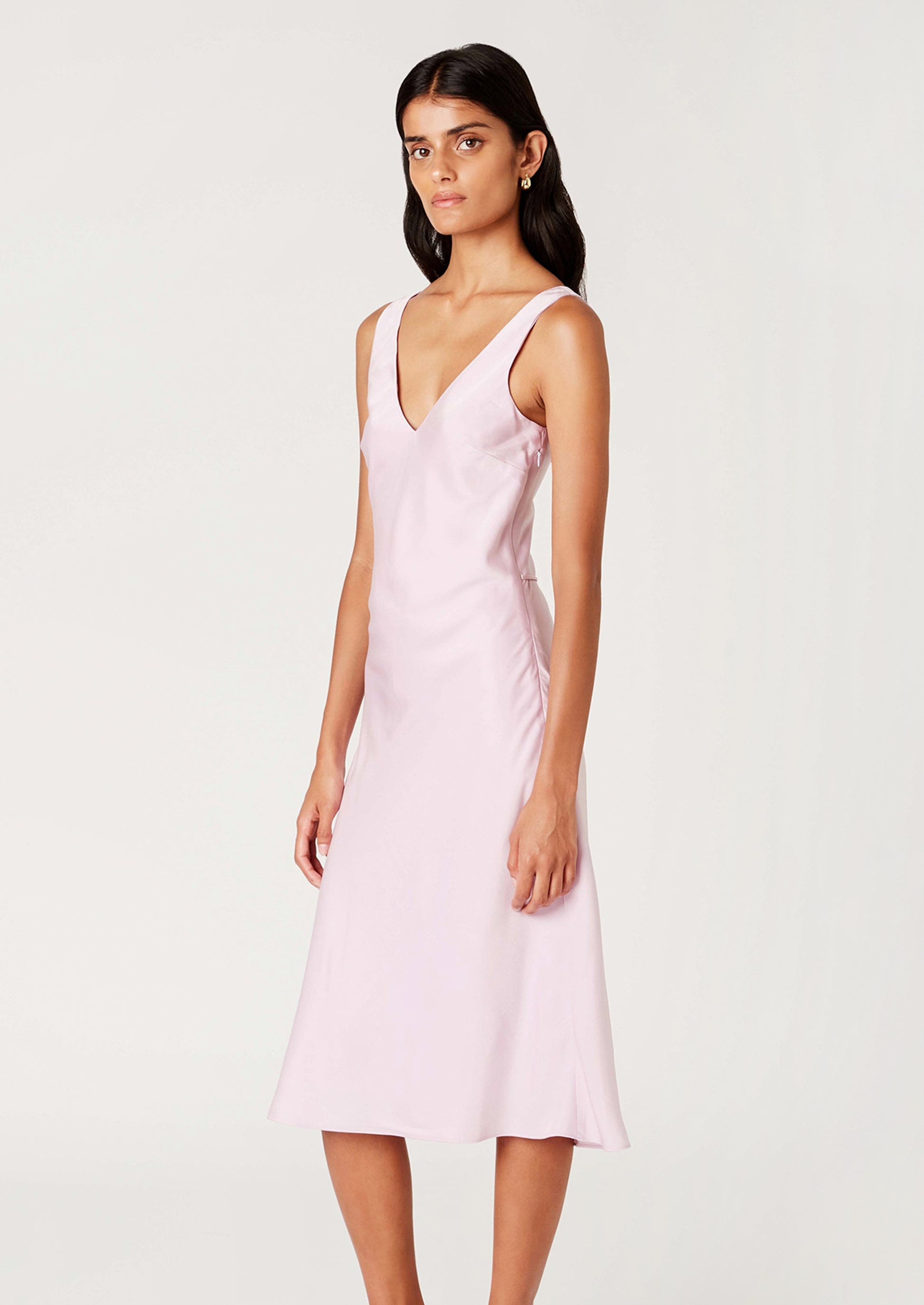 A woman wearing a satin v-neck sleeveless dress in ice pink.