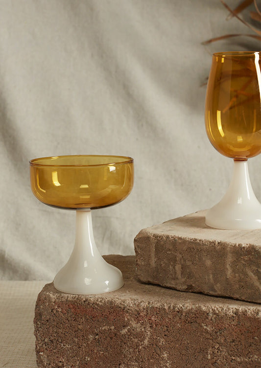 Two amber glass drinkware pieces on a textured surface with a neutral background
