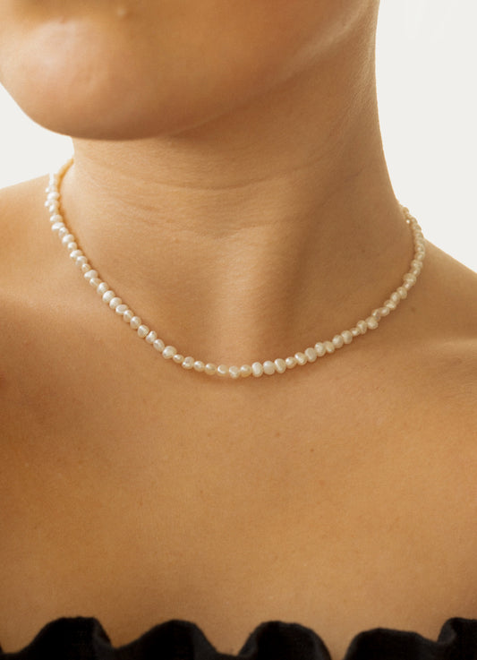 Pearl necklace worn by a person with a neutral background
