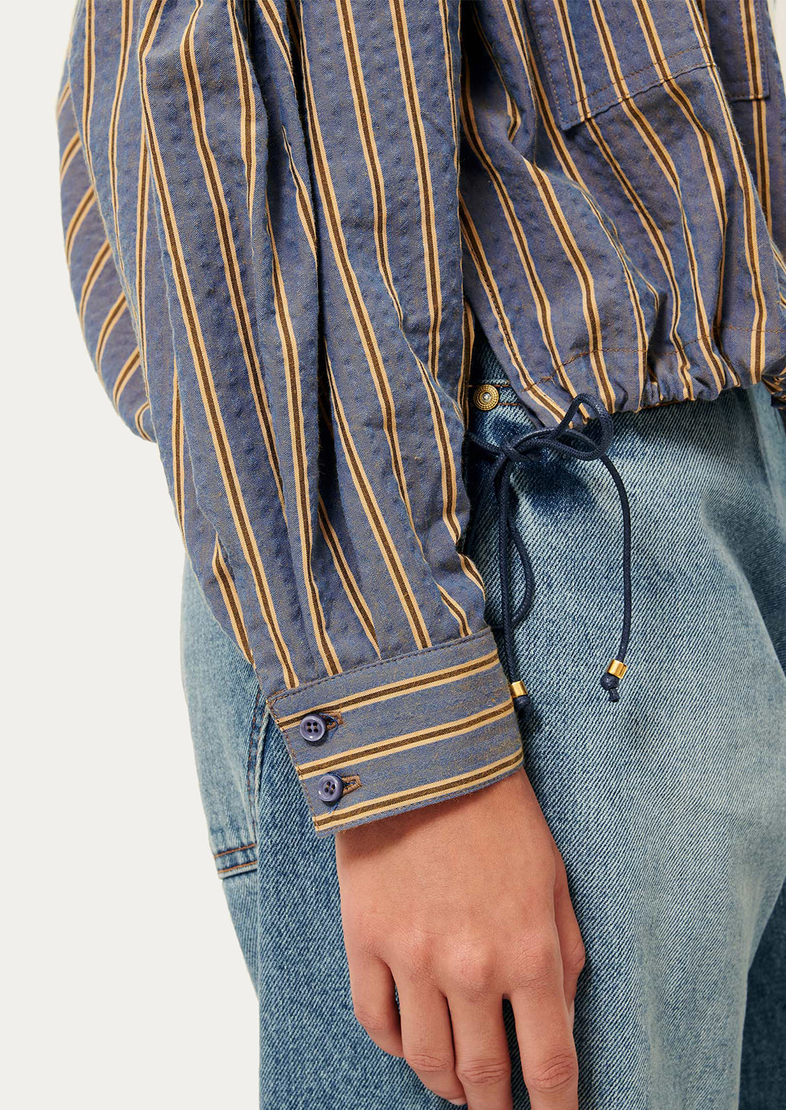 Close-up of a person wearing a striped shirt and jeans with a blurred background