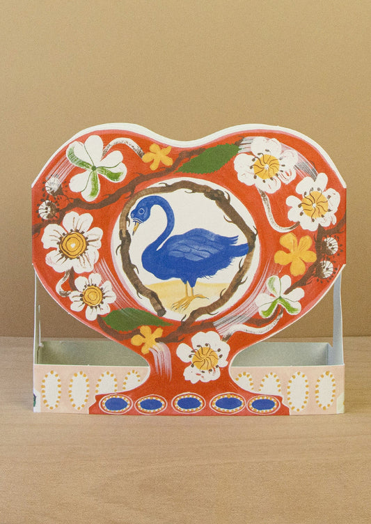 Decorative heart-shaped card with a blue swan and floral design on a beige background