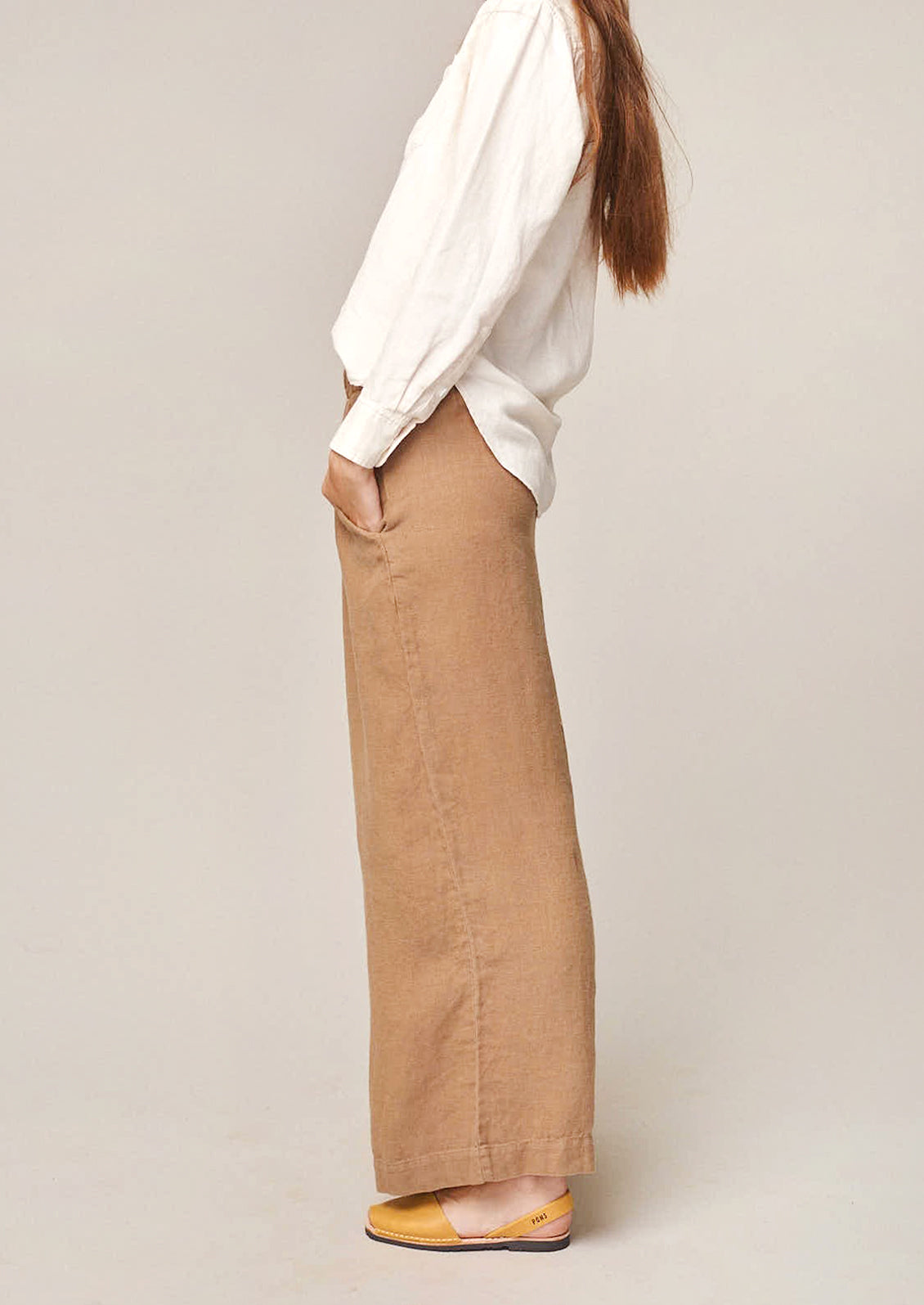 A person wearing a pair of flowy hemp pants in tan.