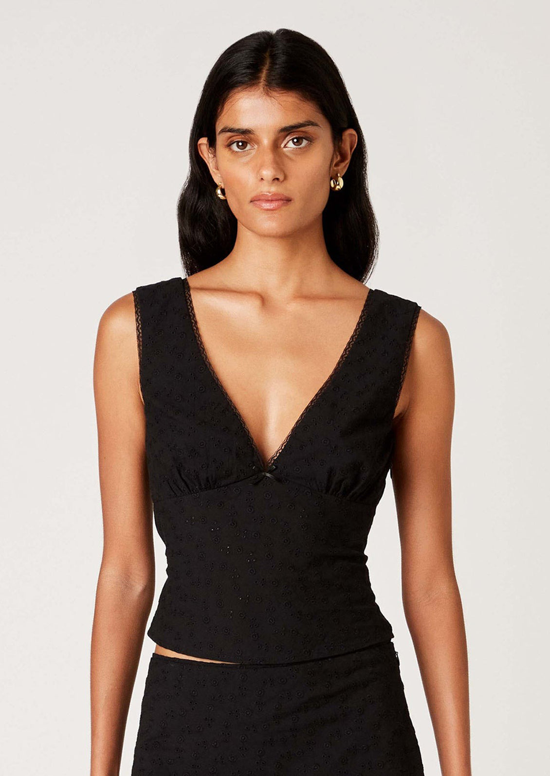 A woman wearing a sleeveless cotton eyelet lace top in black, with deep v-neck.