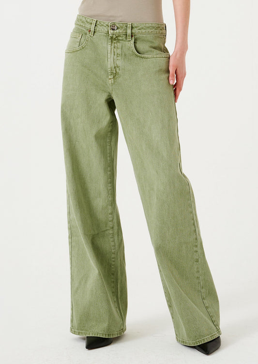 A woman wearing a pair of wide leg jeans in moss green wash.