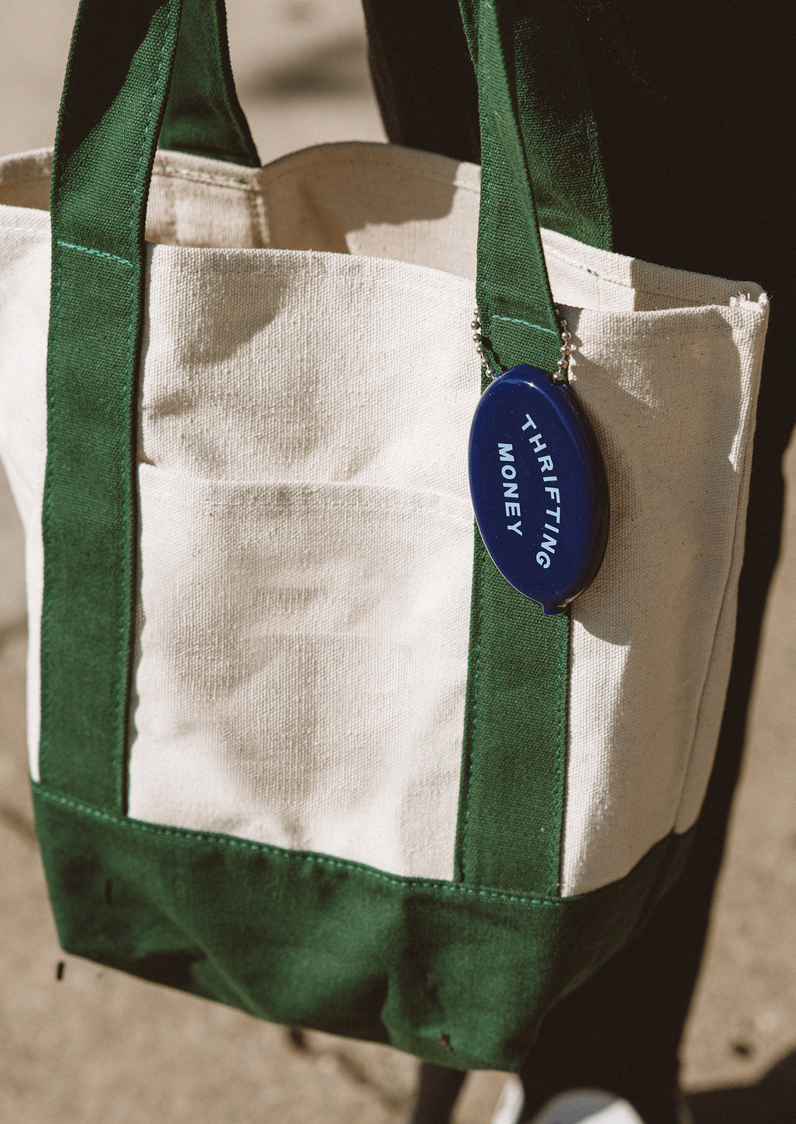 Green and beige tote bag with a blue keychain on a blurred background