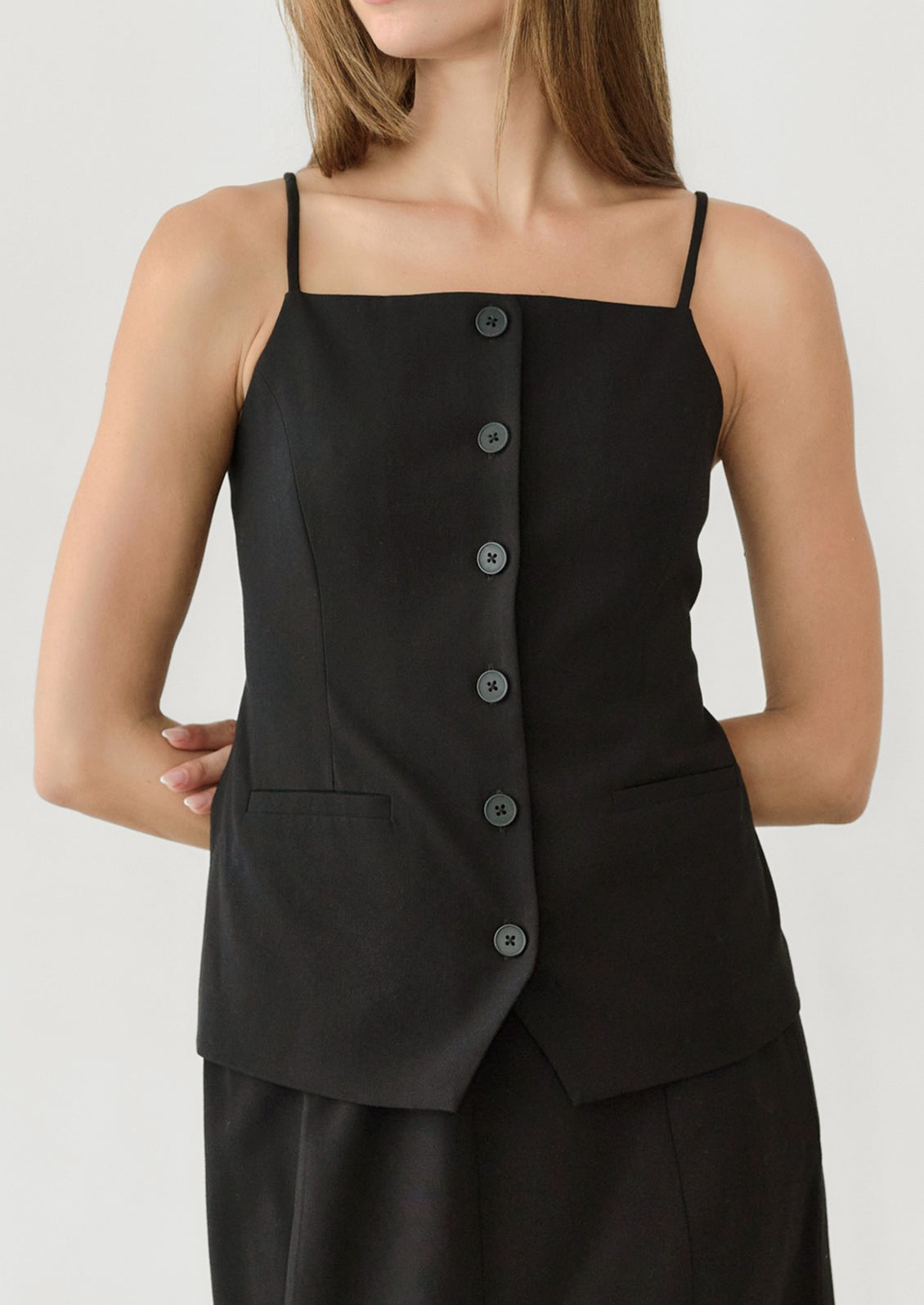 A woman wearing a black vest style top with skinny shoulder straps.