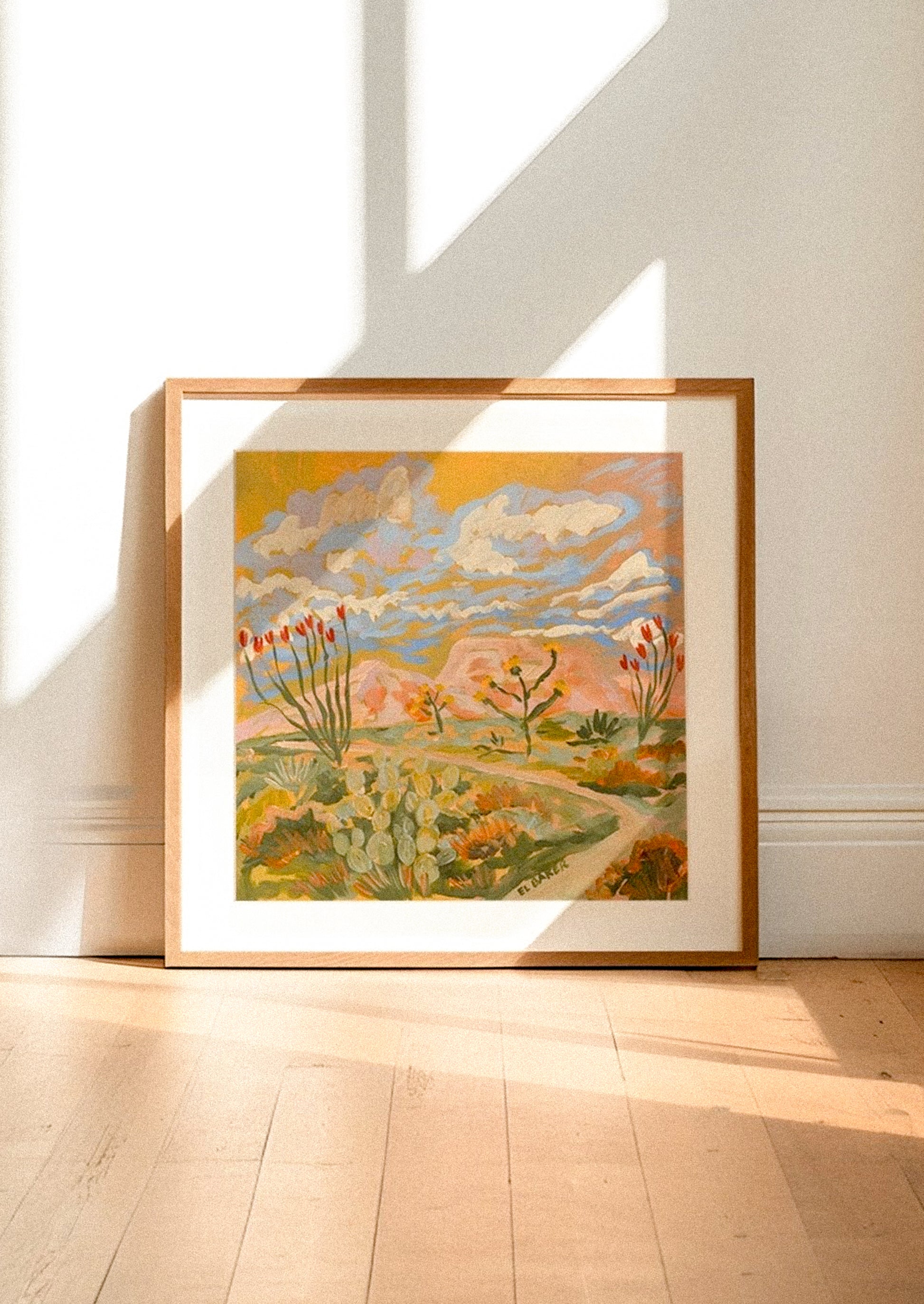 Framed artwork of a landscape with flowers on a white wall.