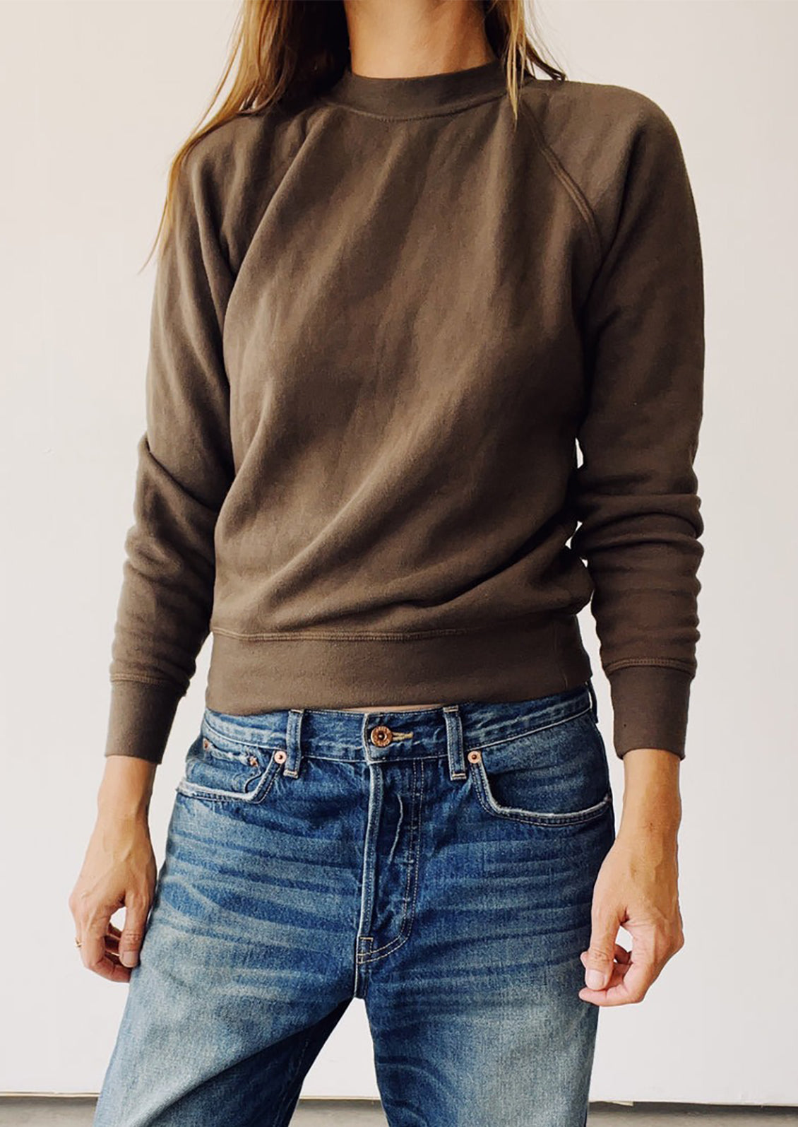 Person wearing a brown sweatshirt and blue jeans against a white background
