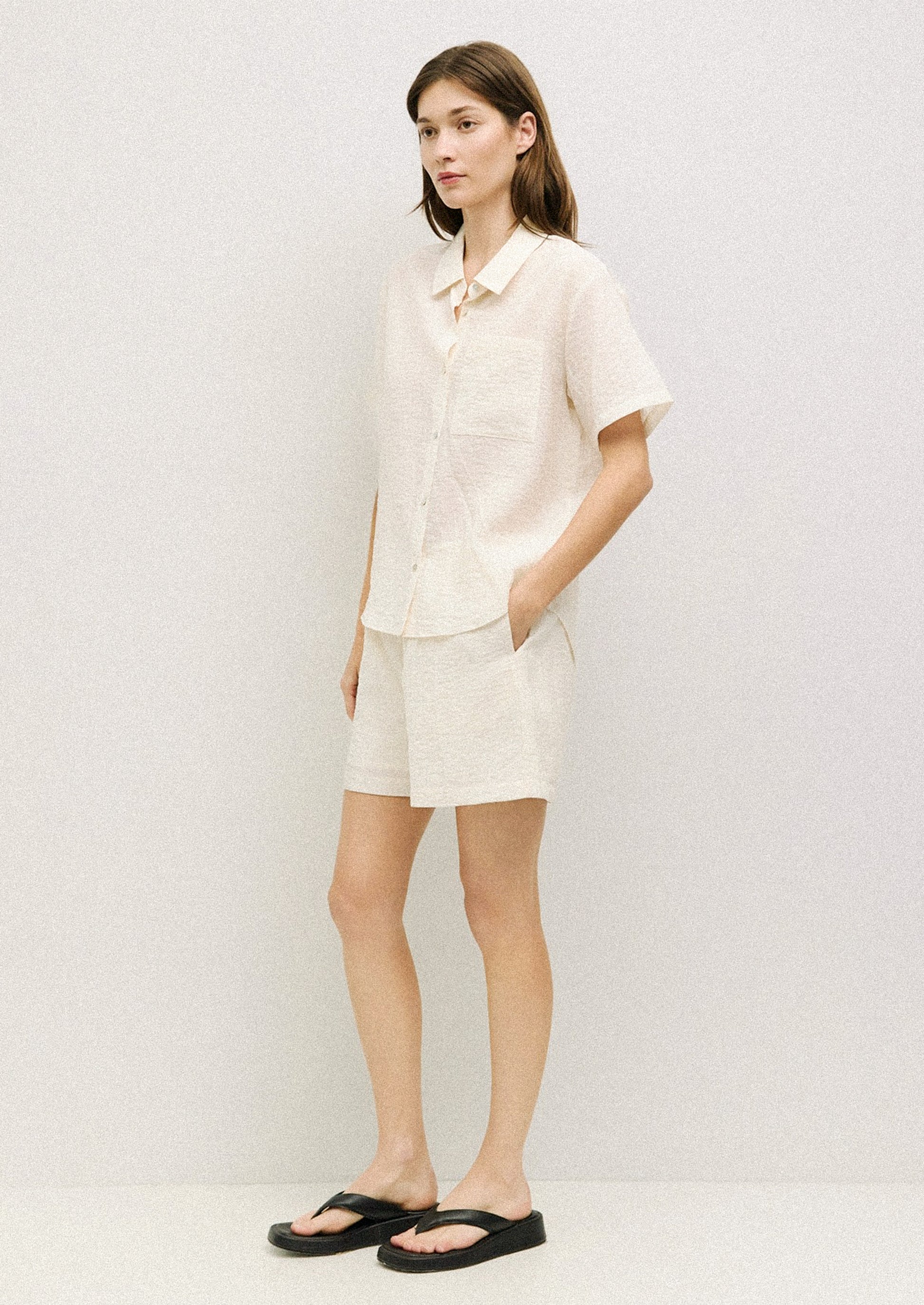 A woman wearing a short sleeve collared button front shirt in cream with soft wrinkled texture.