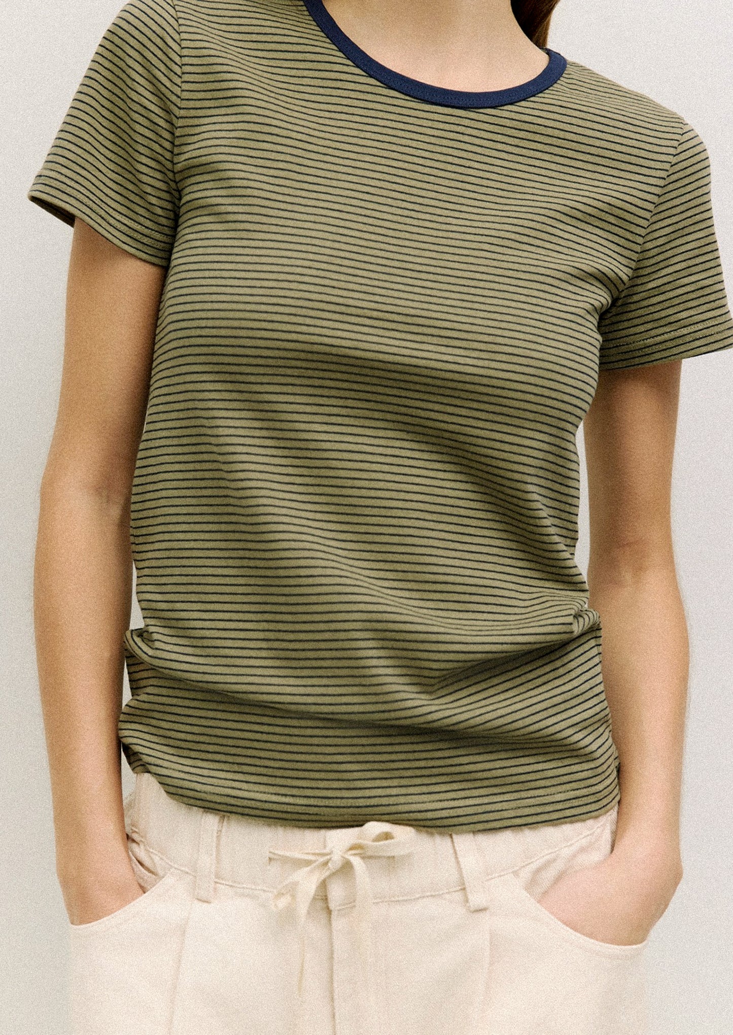 A person wearing a striped t-shirt in olive green with navy stripes and neckline.