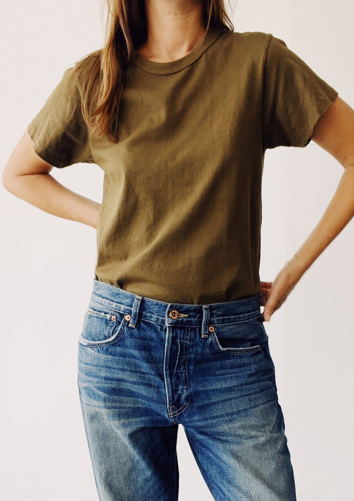 Person wearing an olive green t-shirt and blue jeans on a plain background