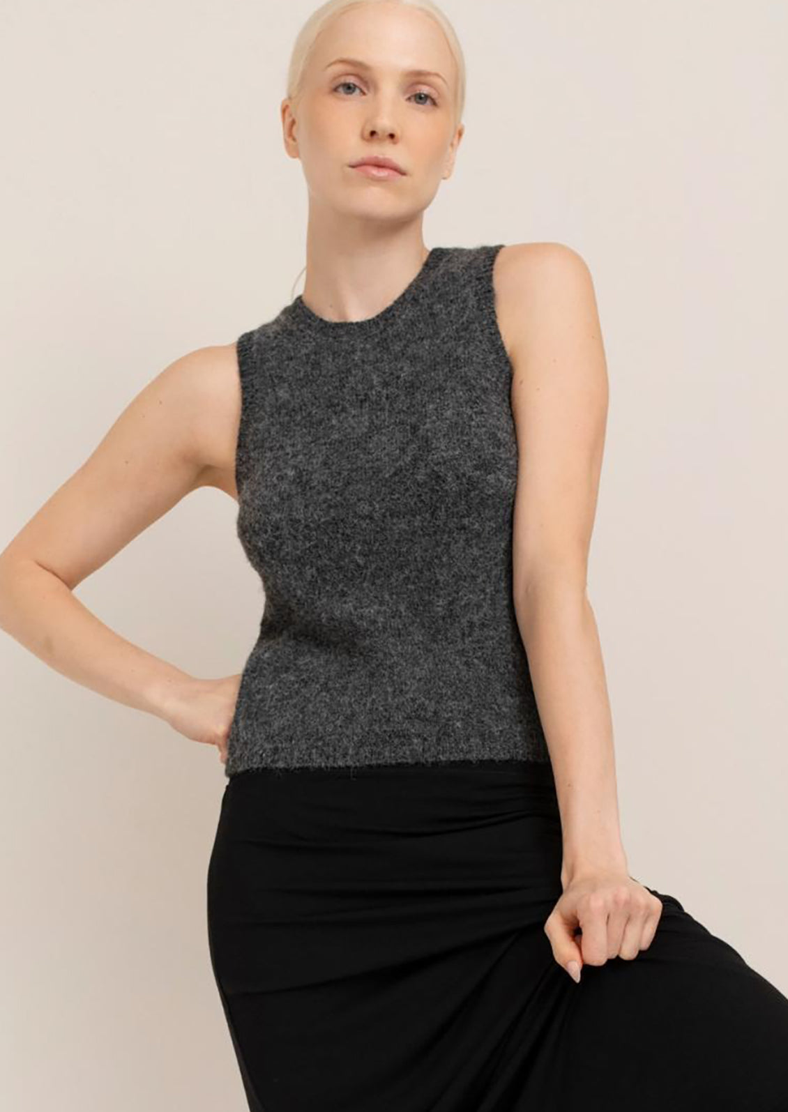 Woman wearing a dark gray sleeveless top and black skirt against a plain background