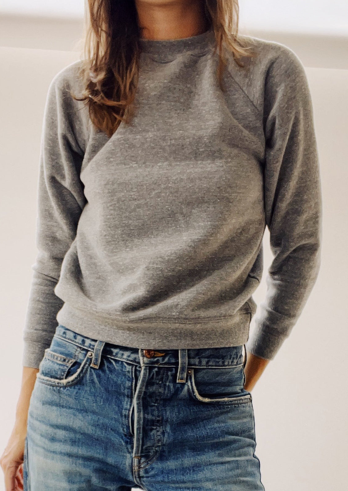 Person wearing a gray sweater and blue jeans against a neutral background
