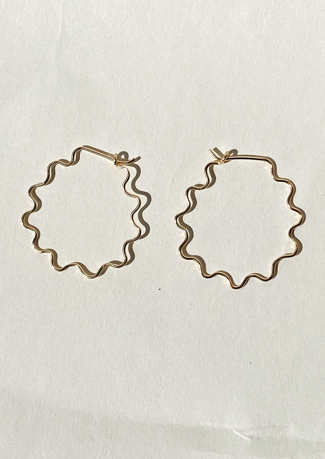 Gold hoop earrings with a wavy squiggle shape on a light beige background.