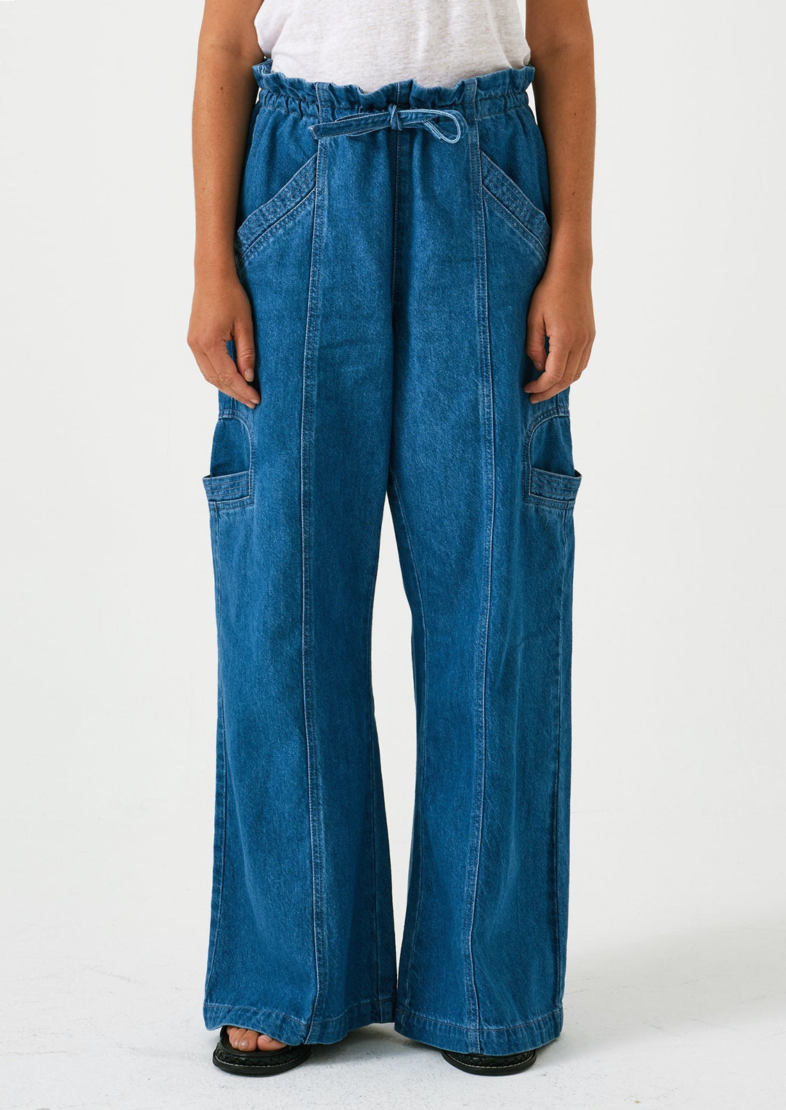 A woman wearing a pair of relaxed leg pants with cargo style details, in bright blue denim.