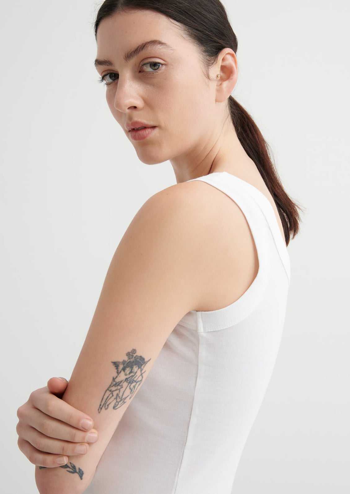 Woman wearing a white sleeveless top against a plain background