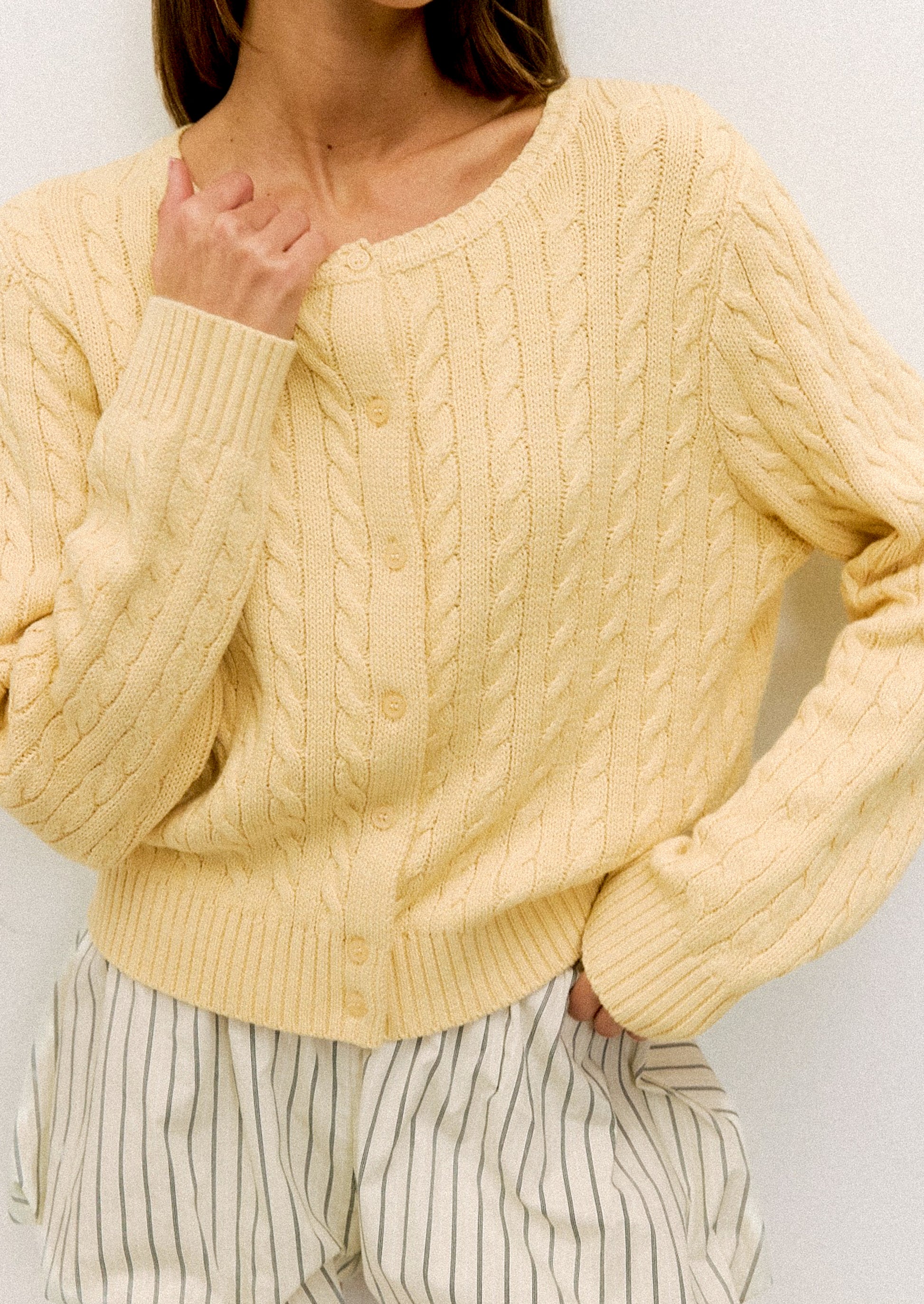 Person wearing a light yellow cable knit sweater against a plain background
