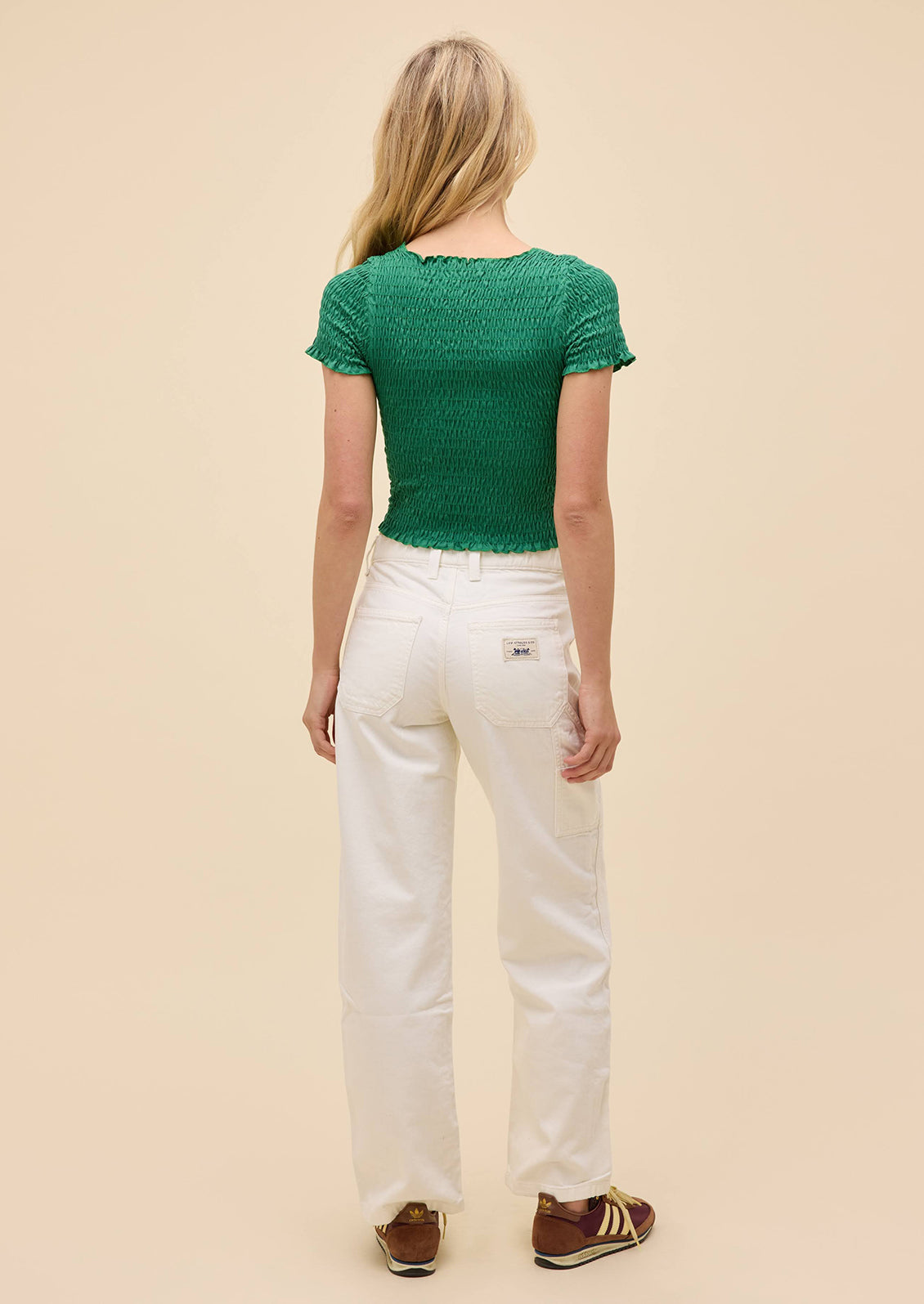 Woman wearing a green top and white pants on a beige background
