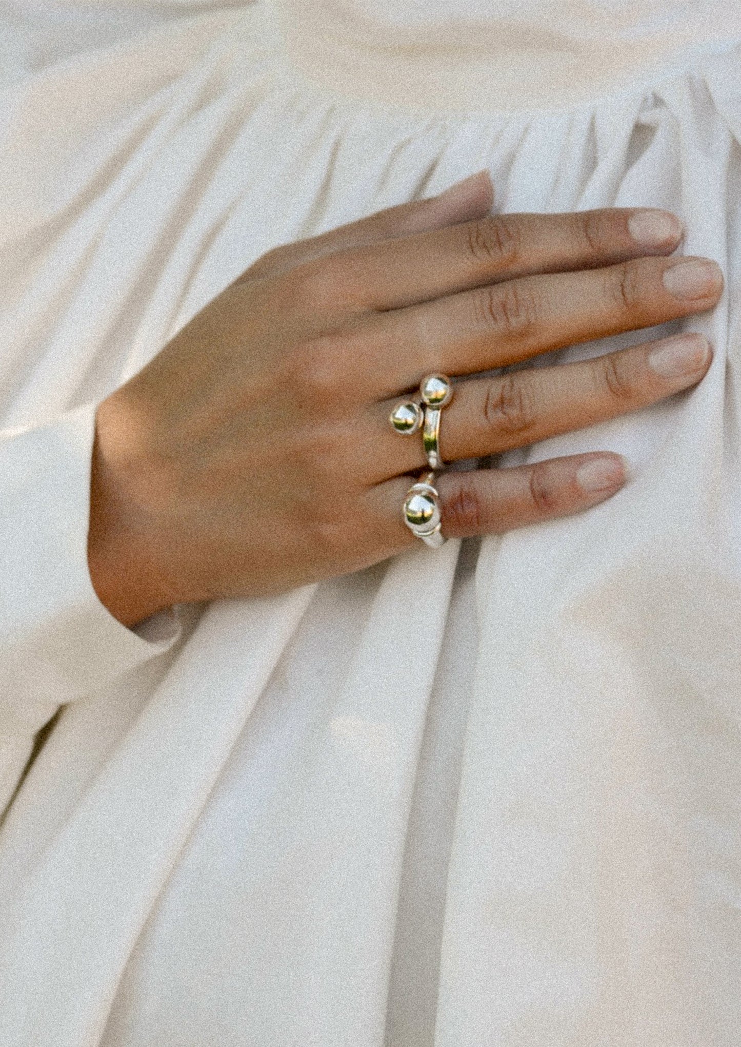 Hand wearing silver rings on a light fabric background