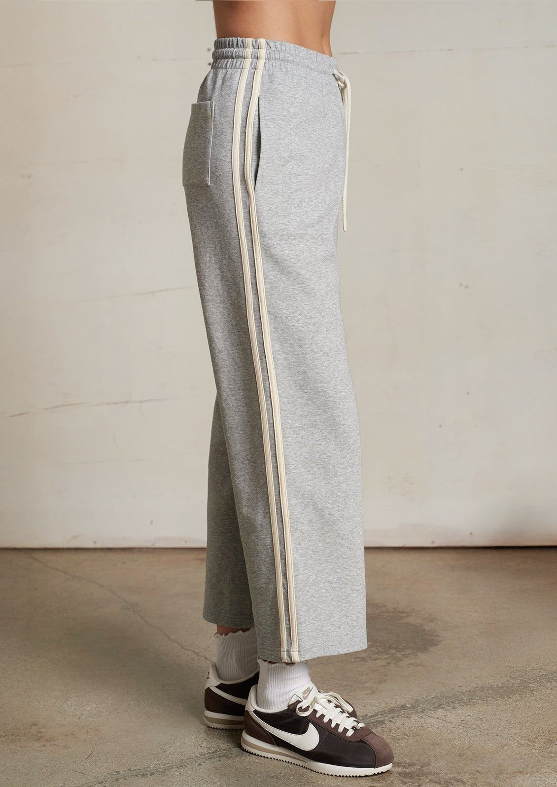 Gray sweatpants with white stripes worn by a person on a plain background