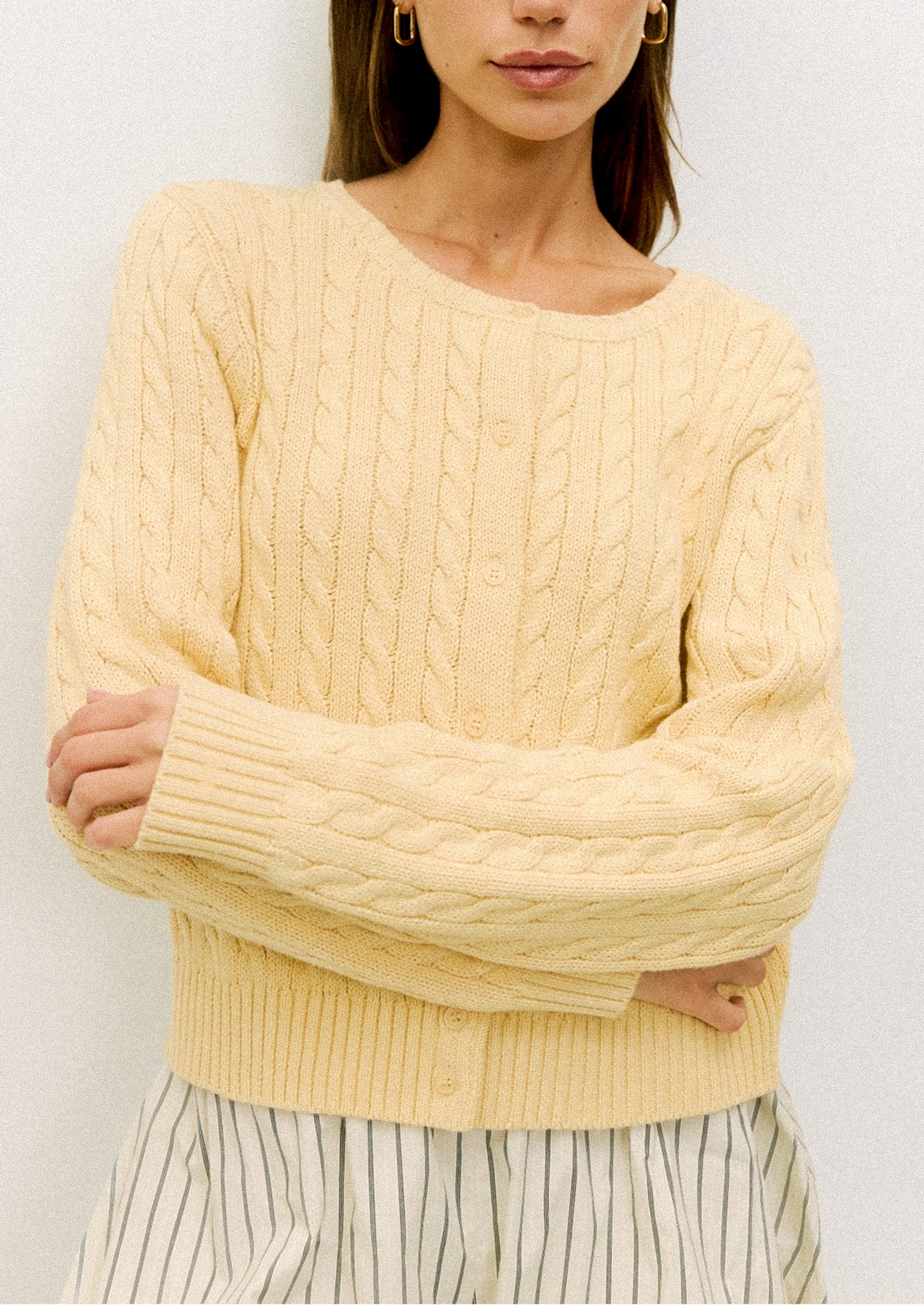 Woman wearing a light yellow cable knit sweater against a white background