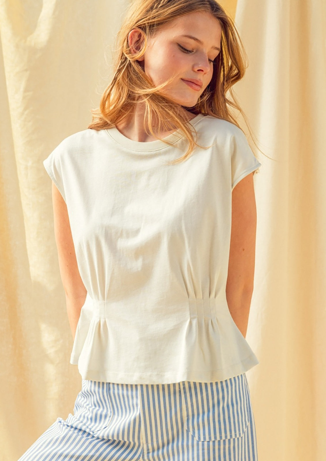 Woman wearing a white sleeveless top with a peplum waist against a beige background