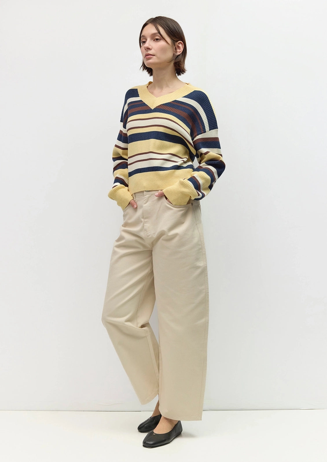 A woman modeling a long-sleeve V-neck knit sweater with navy, mustard yellow, and beige horizontal stripes.
