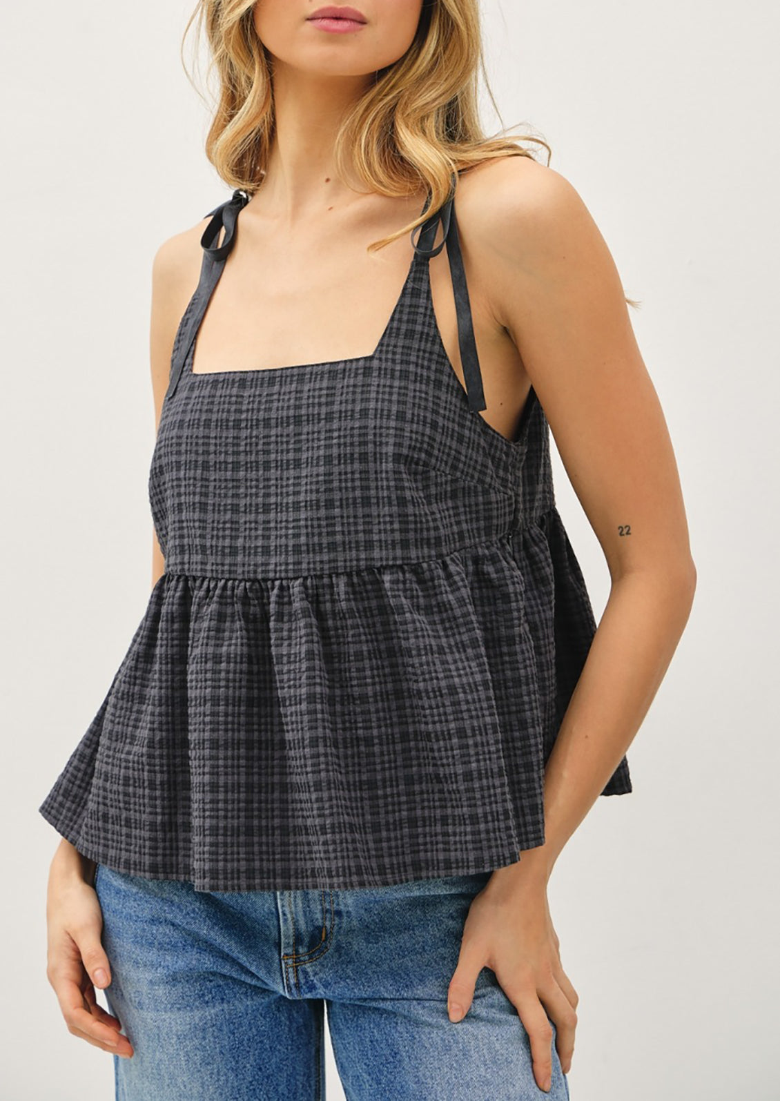 Woman wearing a plaid peplum top and jeans on a plain background