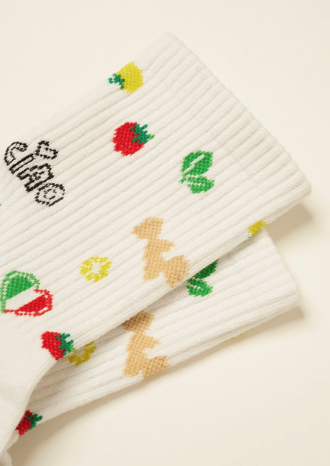 A closeup of a pair of ribbed white socks with fun Italian-inspired illustrations embroidered on them on a cream colored background.