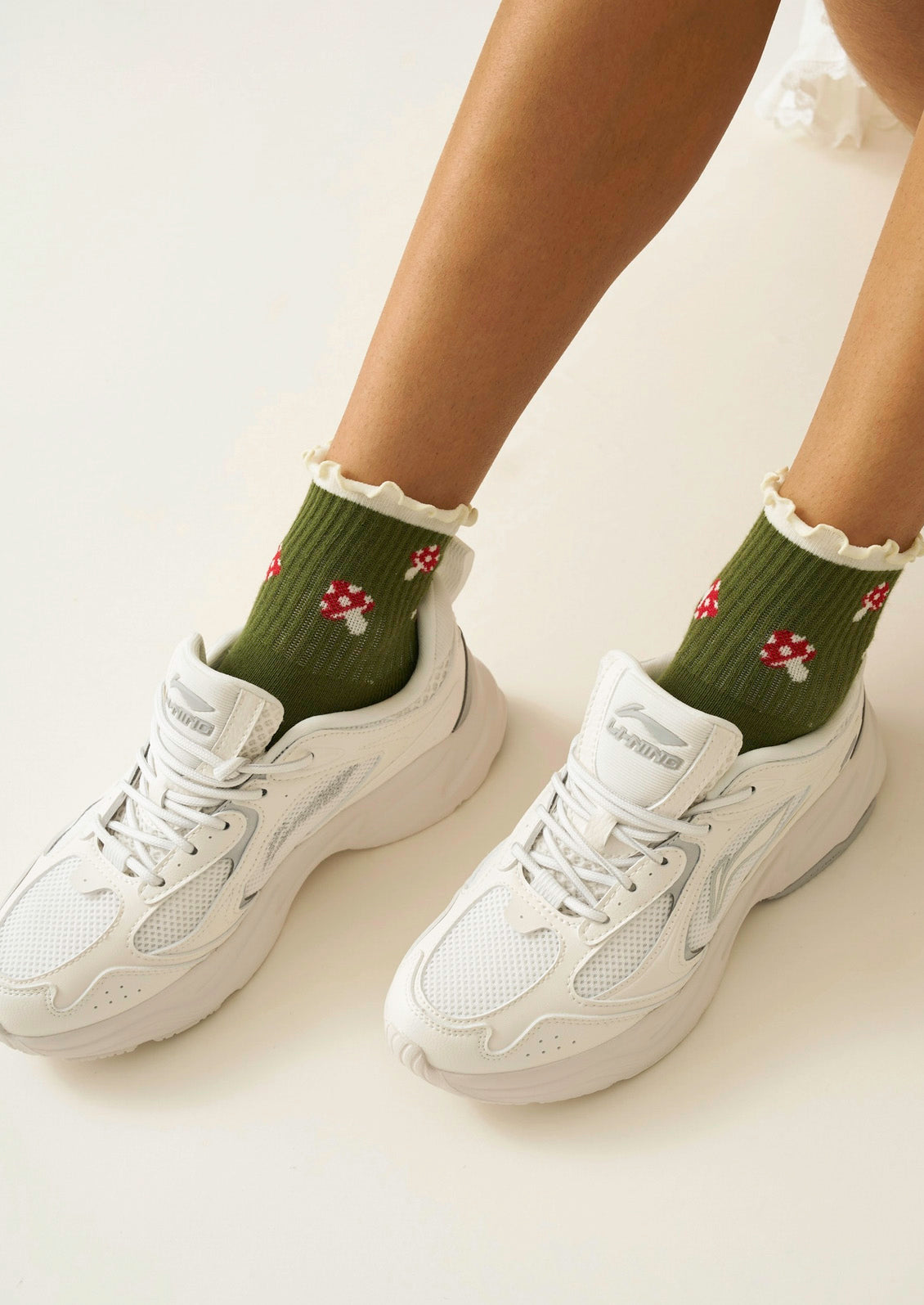 A woman wearing olive green ribbed socks with mushrooms on them and a ruffled trim with white sneakers.
