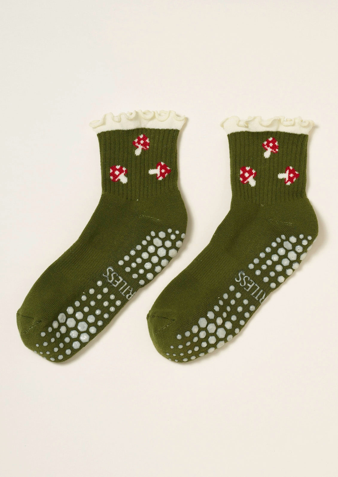 A pair of ribbed olive green socks with red mushrooms embroidered on them, a ruffled trim, and grips at the bottom to prevent slipping.