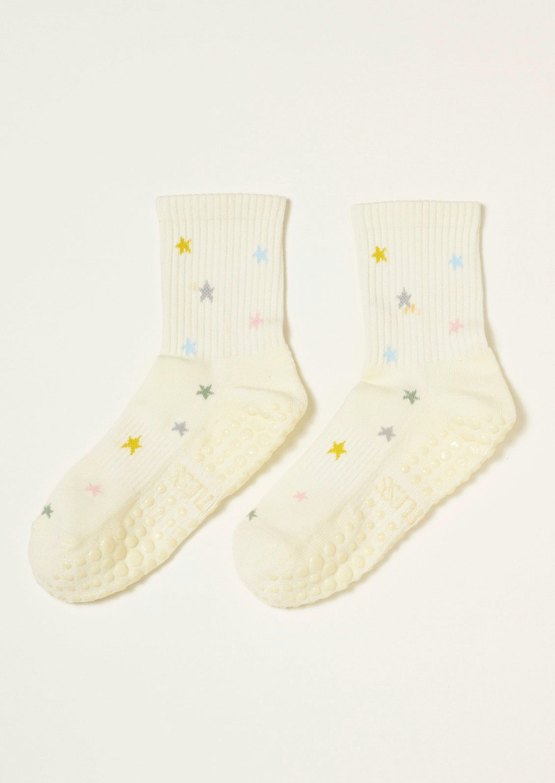 A pair of ribbed cream socks with colorful stars embroidered on them and grips at the bottom to prevent slipping.