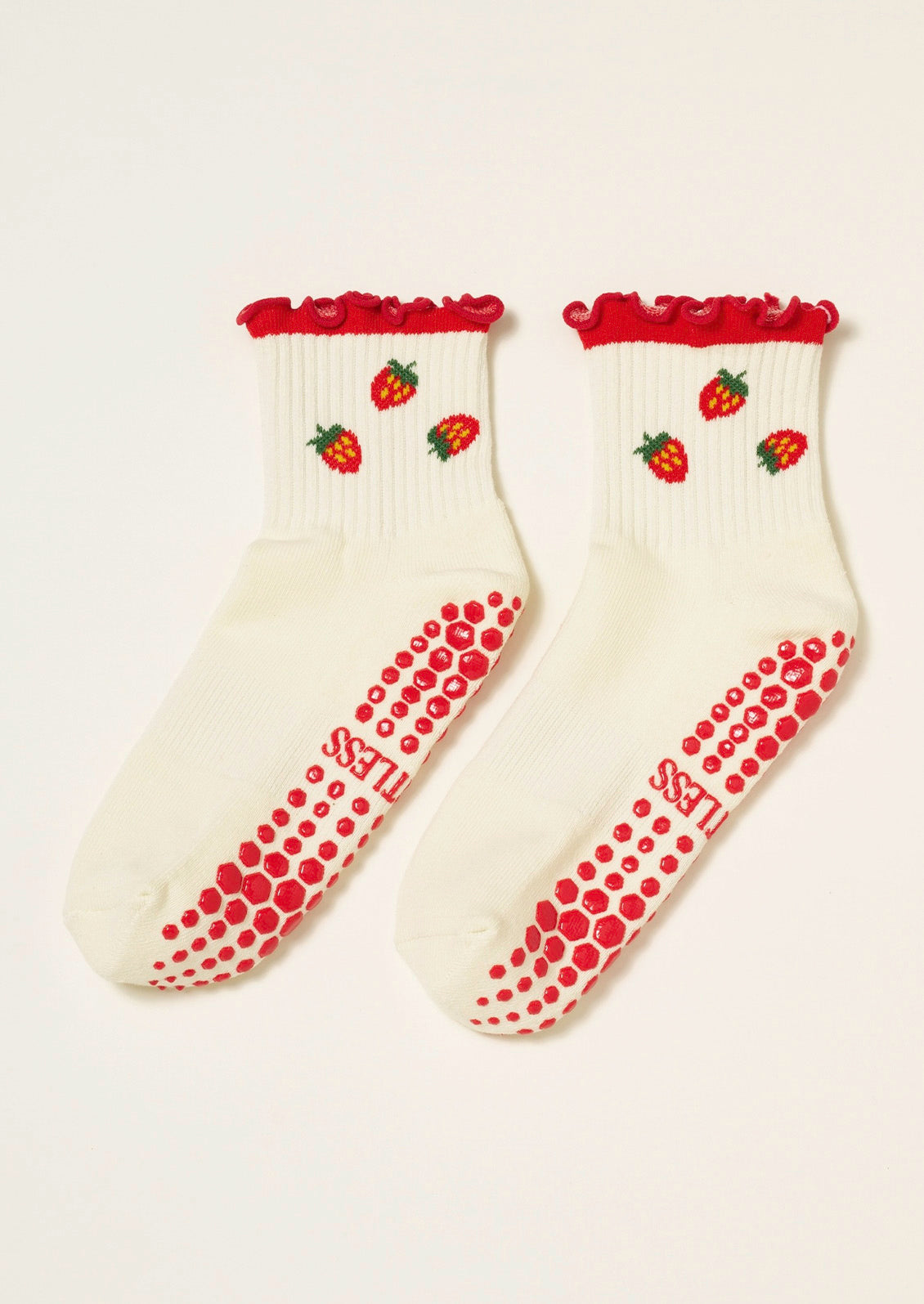 A pair of ribbed cream socks with strawberries embroidered on them, a ruffled trim, and grips at the bottom to prevent slipping.