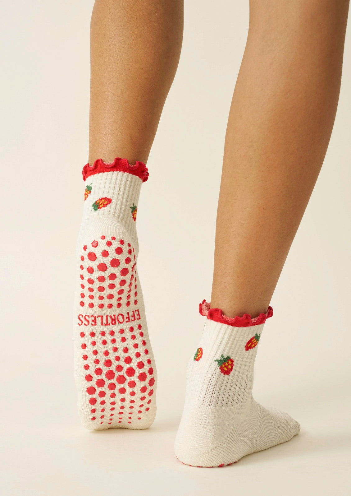 A woman wearing white ribbed socks with strawberries, a red ruffle trim, and grips on the bottom to prevent slipping.