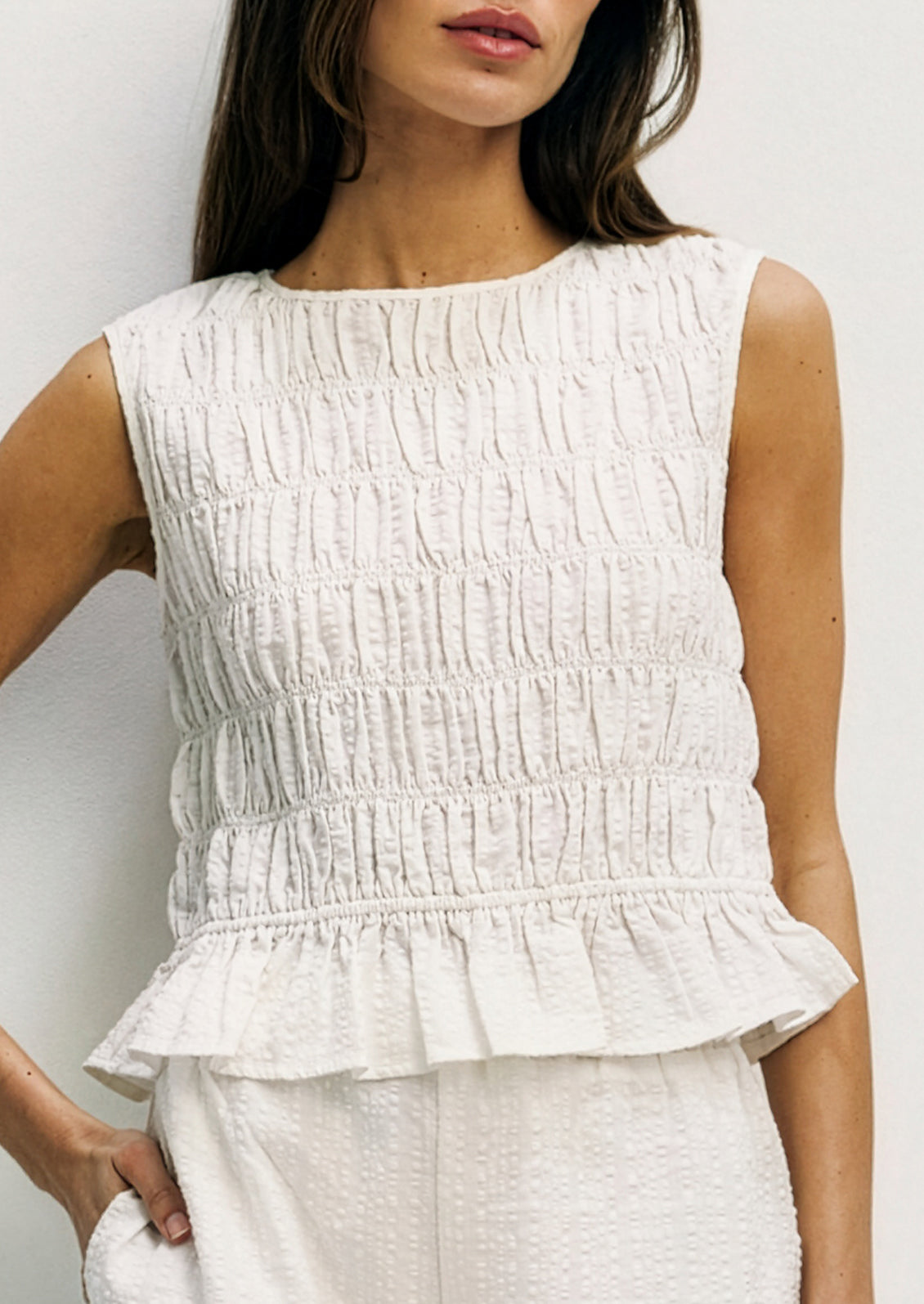 Woman wearing a white textured sleeveless top against a plain background