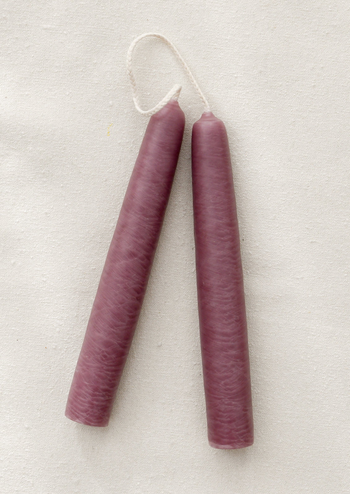 A pair of short mauve taper candles on a brown background.