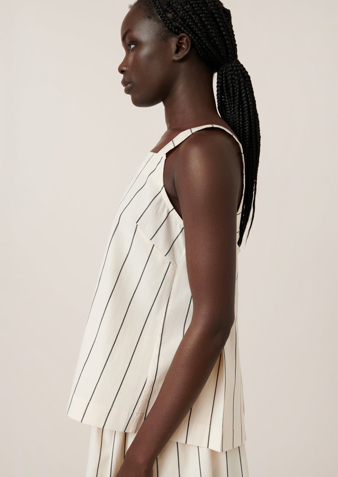 A person wearing a sleeveless top with square neckline, in cream with black pinstripe.