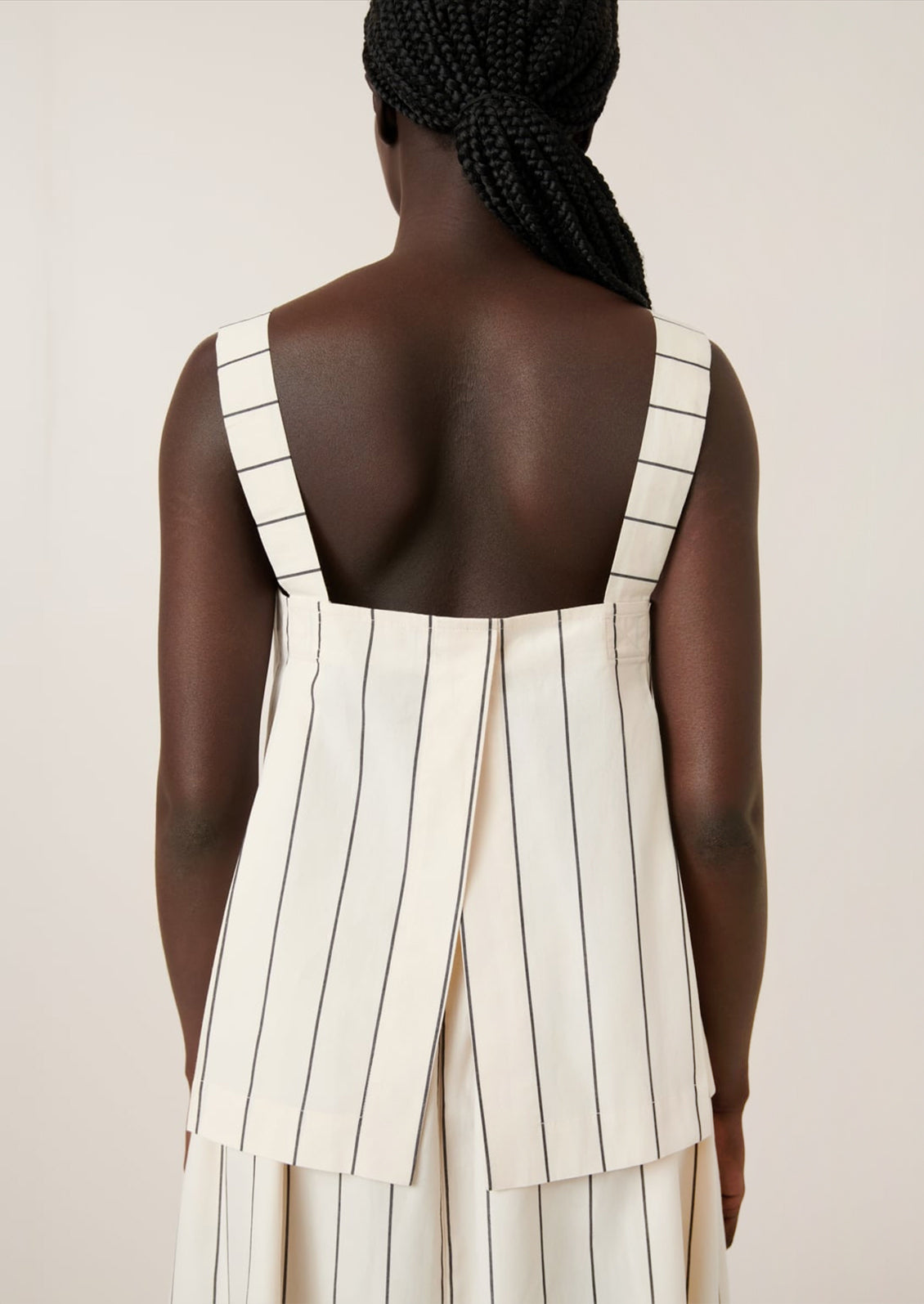 A person wearing a sleeveless top with square neckline, in cream with black pinstripe.